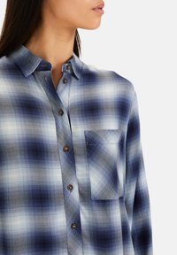 Blauw-witte geblokte overhemden met een button-down kraag, voorzien van bruine knopen en een voorzak. Gemaakt van een geweven, lichtgewicht stof.
