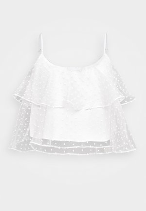 Haut sans manches blanc avec un tissu superposé transparent, présentant un motif texturé à pois et un design ample et fluide.