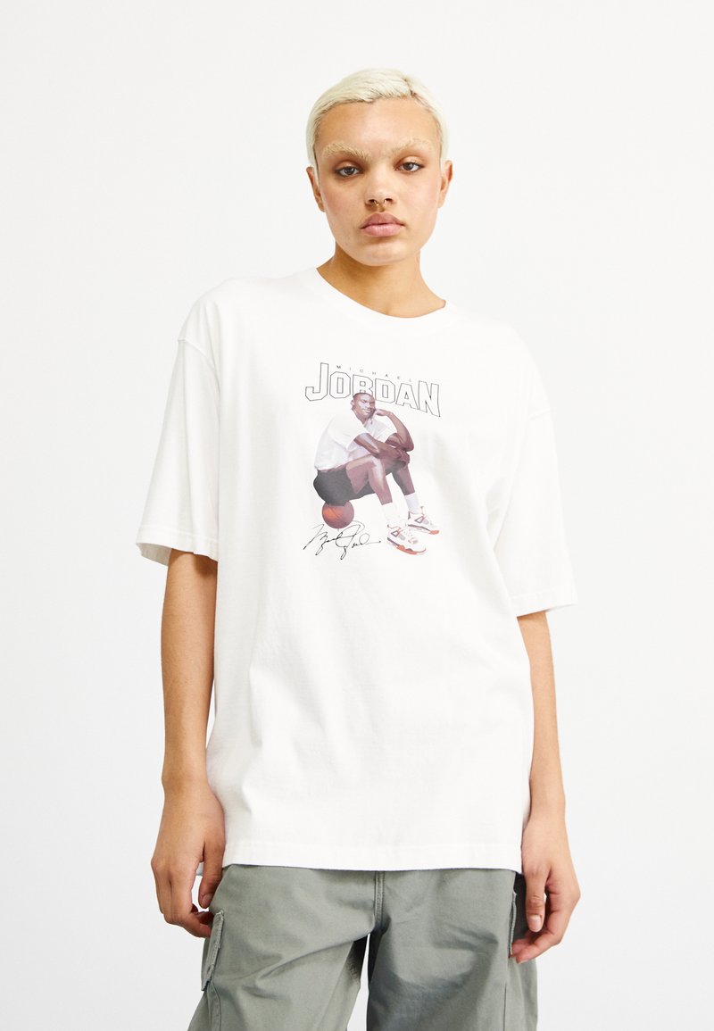 Camiseta blanca de algodón con un gráfico de Michael Jordan sentado sobre un balón de baloncesto, con la palabra "JORDAN" y una firma en la parte inferior.