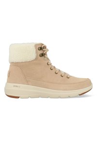 Beige suède enkellaarzen met een pluizige witte rand, ronde neus en metalen oogjes. Dikke roomkleurige zool met het label "ULTRA GO."