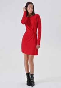 Rode jurk met lange mouwen, voorzien van een gedraaide taille en een licht uitlopende zoom; gladde, lichte stof met een aansluitend silhouet.