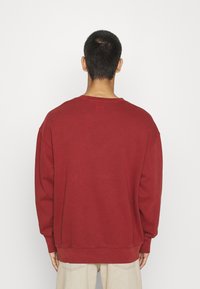 Felpa color bordeaux in misto cotone, con vestibilità comoda, spalle scese e polsini a costine. Design semplice senza motivi o accenti.