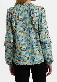 Květinová blůza s modrými, žlutými a hnědými vzory, s volánovými rukávy a nařaseným výstřihem, vyrobená z lehké, texturované látky.
