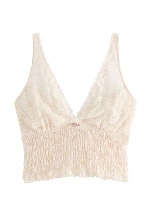 Kermanvärinen pitsinen bralette, jossa on rypytetty vyötärö, laskosreunat ja pieni vaaleanpunainen ruusukoriste keskellä edessä.