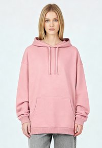 Roze capuchontrui gemaakt van zachte stof met een voorvak, doorgezakte schouders en geribbelde manchetten en zoom. Eenvoudig ontwerp.