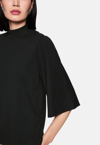 Black high-neck top with short, bell sleeves, made from a smooth fabric. Features a relaxed fit and minimalistic design.