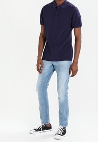 Polo shirt marine à manches courtes, patte de boutonnage à deux boutons, jeans bleu clair et baskets en toile noires avec semelles blanches.