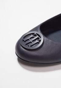 Nawękowa skórzana baletka w kolorze granatowym z okrągłym czarnym logo na palcu. Gładka faktura z delikatnym połyskiem i zaokrąglony kształt.