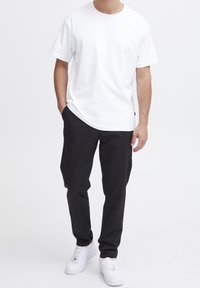 Bílé bavlněné tričko s krátkými rukávy, doplněné o černé kalhoty a bílé tenisky. Tričko má kulatý výstřih a volný střih.