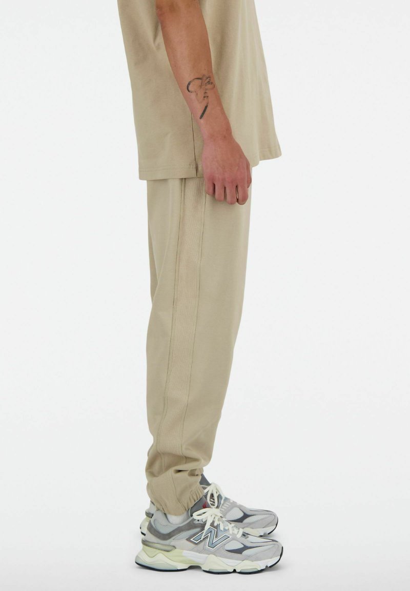 Jogging en beige en tissu doux, avec des coutures latérales et une taille élastique, associés à des chaussures de sport grises et vert clair.
