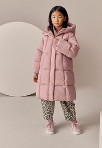 Rosa puffjakke med hætte, syede paneler og lynlås foran. Kombineret med leopardmønstret bukser og rosa sneakers med snørebånd.
