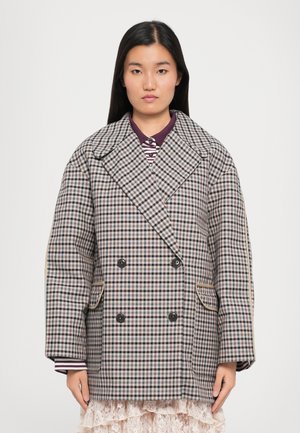 Dubbelzijdige gecheckte coat in bruin, crème en blauw. Kenmerkt zich door grote revers, twee voorzakken en contrasterende streepdetails op de mouwen.