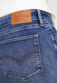 Primer plano del bolsillo trasero de unos jeans Levi's azules y la etiqueta de cuero de la marca sobre una persona que lleva una camisa blanca.