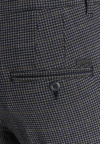 Námořnické kostkované kalhoty s jemným vzorem houndstooth, zadní kapsou s černým knoflíkem a texturovaným povrchem.