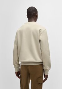 Beige pulóver, kerek nyakkivágással, bordás mandzsettákkal és aljjal; puha, sima textúrájú anyagból készült. Kényelmes illeszkedés és hátsó nézet.