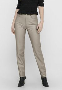 Beige aansluitende broek van een soepele, rekbare stof. Heeft een middelhoge taille, voorzakken en een standaard knoop- en ritssluiting.