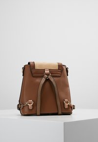 Brown leather backpack with a textured top panel, gold hardware accents, and a drawstring closure, featuring adjustable straps and a structured shape.