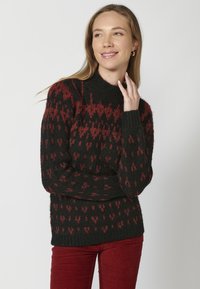 Pull en tricot noir avec des motifs géométriques rouges, col montant et poignets et ourlet côtelés. Texture douce, coupe décontractée et longueur moyenne.