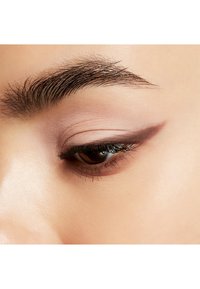 Acercamiento a un ojo con sombras de ojos rosa suave, delineador de ojos marrón oscuro en ala, pestañas prominentes y cejas bien cuidadas.