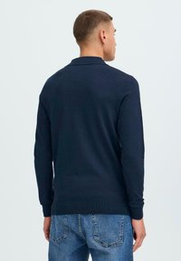 Marineblå genser med krage, ribbestrikkede mansjetter og kant. Stoffet ser glatt ut med en tettsittende design.
