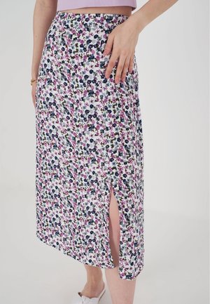 Kvinde iført en hvid midi nederdel med blomsterprint i lilla, blå og grøn samt en frontslids, kombineret med en lyse lilla cropped top.