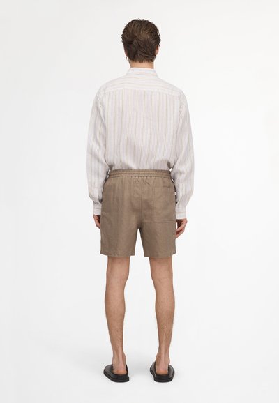 Personne portant une chemise à manches longues rayée, un short beige à taille élastique avec une poche arrière et des sandales noires à enfiler, vue de dos.
