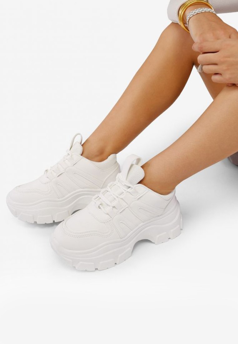 Zapatillas blancas con suela gruesa, paneles texturizados y cordones, con una lengüeta en la parte trasera para facilitar su uso. Material sintético suave.