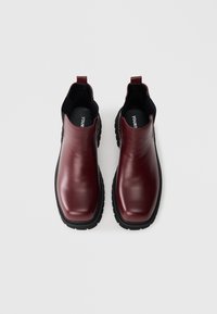 Viininpunaiset nahkaiset Chelsea-saappaat, joissa on sileä pinta, joustavat sivupaneelit ja mustasta kumi-materiaalista valmistettu, kuvioidulla urituksella varustettu pohja.