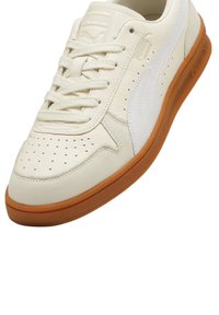 Sneaker bianca in pelle con punta perforata, suola in gomma marrone e striscia bianca laterale. Presenta lacci e logo impressa sulla linguetta.