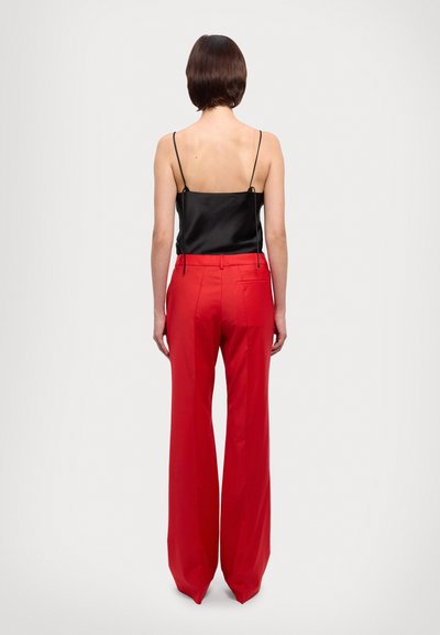 Black satin camisole with thin straps paired with high-waisted, wide-leg red trousers featuring side pockets and a back pocket detail.