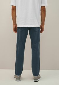 Pantaloni blue straight-leg cu o textură netedă, buzunare la spate și cusături subtile, asortați cu adidași gri și un tricou alb.