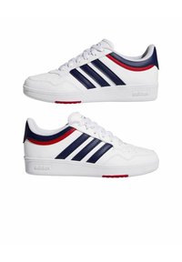 Zapatillas blancas con tres franjas azul marino y detalles en rojo. Fabricadas con material sintético, cuentan con una suela plana y cierre de cordones.