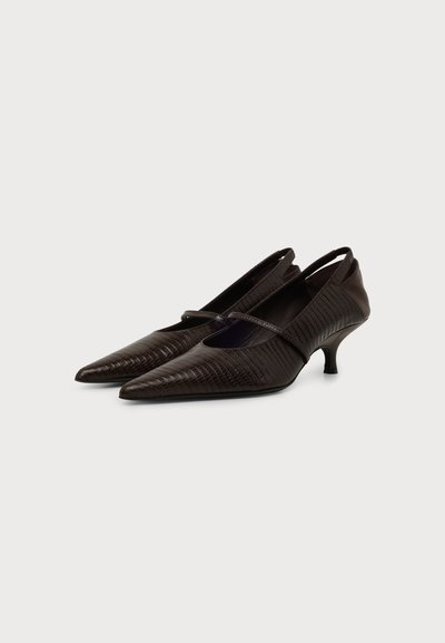 Paire de chaussures à petit talon en cuir brun foncé texturé avec des bouts pointus et une fine bride sur le dessus, sur un fond clair.
