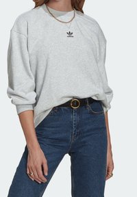 Grå sweatshirt med rundad halsringning och svart Adidas-logotyp, kombinerad med mörkblå högmidjade jeans och ett svart bälte med ett guldspänne.