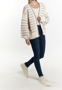 Cardigan en maille crème avec des rayures lavande, manches surdimensionnées et ourlet côtelé. Associé à un jean foncé et des baskets blanches.