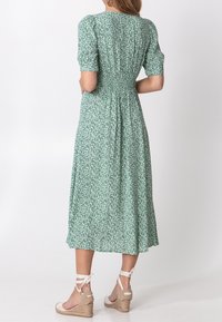 Green floral midi dress with puff sleeves, smocked waist, and a flowing skirt. Worn with tan espadrille sandals, featuring ankle ties.