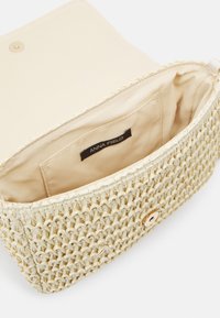 Torebka kopertówka z plecionego słomy w jasnobeżowym kolorze, z gładkim materiałowym wnętrzem i złotym zatrzaskiem. Wnętrze z widoczną kieszonką wsuwaną.