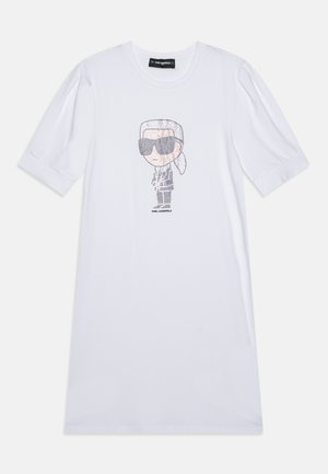 Vestido de algodón blanco con un gráfico de dibujos animados con gafas de sol. Mangas cortas abullonadas y un corte relajado. Textura suave, diseño sencillo.