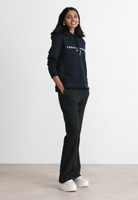 Granatowy hoodie z logo i sznurkiem, w połączeniu z czarnymi spodniami i białymi trampkami na platformie. Gładka tekstura, luźny krój, minimalistyczny design.