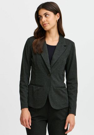 Tmavě šedý blazer vyrobený z texturované látky, s jedním tlačítkem, klopami ve tvaru "notch" a dvěma předními kapsami. Nosený přes černou košili.