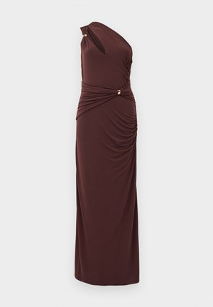 Asymmetrische bruine jurk van zachte stof, met gedrapeerde details bij de taille en accenten in goudkleurig metaal. Lange, nauwsluitende silhouet.