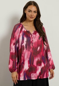 Langärmlige Bluse mit einem pinken und lila abstrakten Muster; verfügt über einen geknöpften Henley-Ausschnitt und geraffte Ärmelbündchen; leichtes Material.