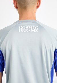 Šedé a modré sportovní tričko s krátkým rukávem, hladkým povrchem a nápisem "COSMIC DREAMS" vytištěným bílou barvou na zádech.