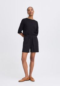 Haut en tricot noir à manches courtes, associé à un short noir à cordon de serrage. Des mocassins beiges avec des accents en métal complètent la tenue.