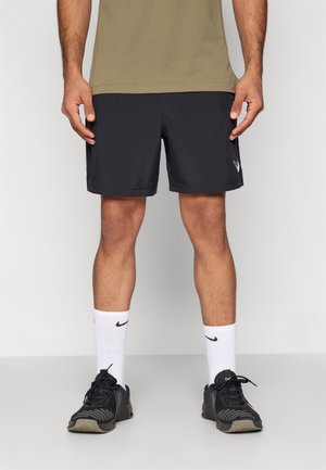 Pantalones cortos atléticos negros con un diseño aerodinámico, combinados con calcetines blancos acanalados con un logo negro y zapatillas negras con textura.