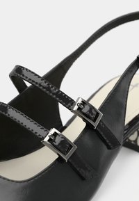 Černé kožené sandály s dvěma nastavitelnými popruhy se čtvercovými kovovými přezkami, texturovaným povrchem a uzavřenou špičkou.