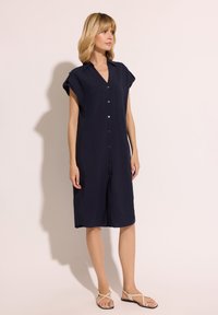 Granatowa lniana sukienka z krótkimi rękawami, zapinana na guziki, z rozcięciami po bokach. Zestawiona z cielistymi płaskimi sandałami. Gładka tekstura, luźny krój.