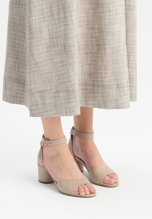 Sandali con tacco in pelle beige, con punta aperta, cinturino alla caviglia regolabile e tacco a blocco. Finitura liscia e design minimalista.