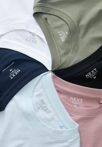 Six t-shirts de marque NEXT, coupe slim et taille moyenne, pliés, dans les couleurs blanc, olive, noir, marine, bleu clair et rose, disposés en cercle.