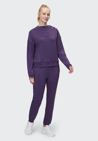 Lila Sweatshirt und passende Jogginghosen aus weichem Stoff. Das Sweatshirt ist mit "VENICE BEACH" geprägt und hat dekorative Knöpfe auf der Schulter.